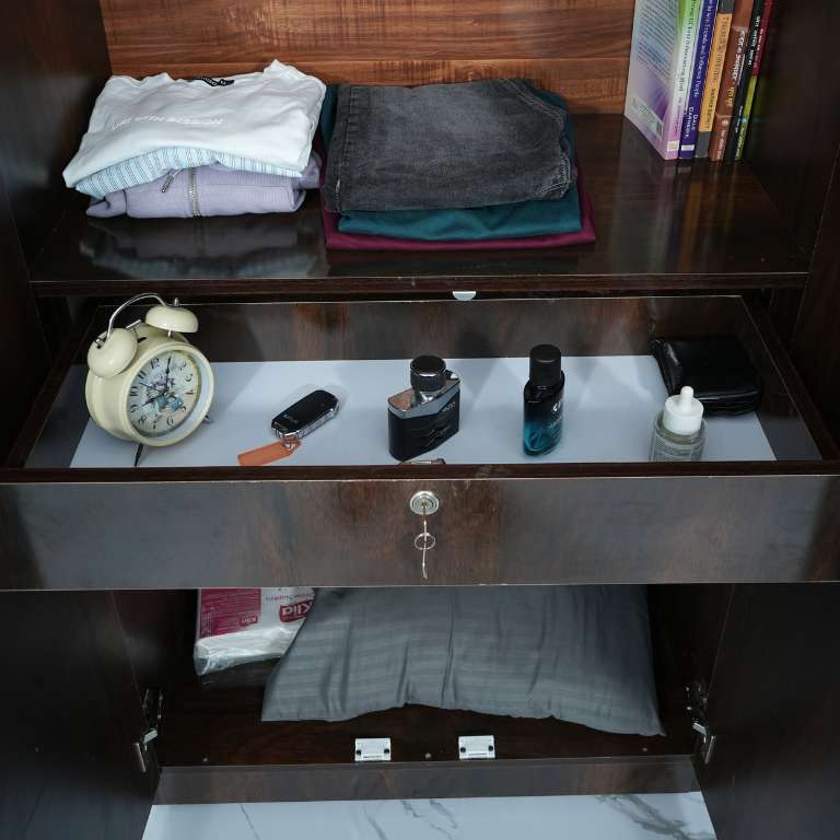 Open drawer with clothes, alarm clock, and personal items in a two door wooden wardrobe.