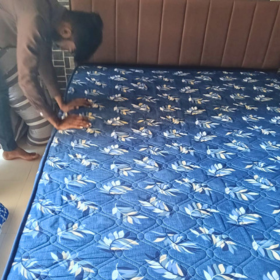 Free delivery and pickup for home furniture and appliances all across pune. A person is adjusting a blue quilted mattress cover with a white floral pattern on a bed with a brown headboard. Available on affordable monthly rent with free delivery in pune kharadi wagholi Hadapsar Amanora Magarpatta keshav nagar Viman Nagar Aundh Baner Balewadi Hinjewadi Wakad ravel punawale.